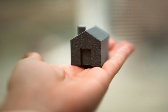 A small, dark gray house model rests in the palm of a hand, symbolizing property investment and CRE portfolio growth.