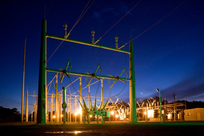An illuminated electrical substation at dusk with power lines, representing critical infrastructure for energy investment.