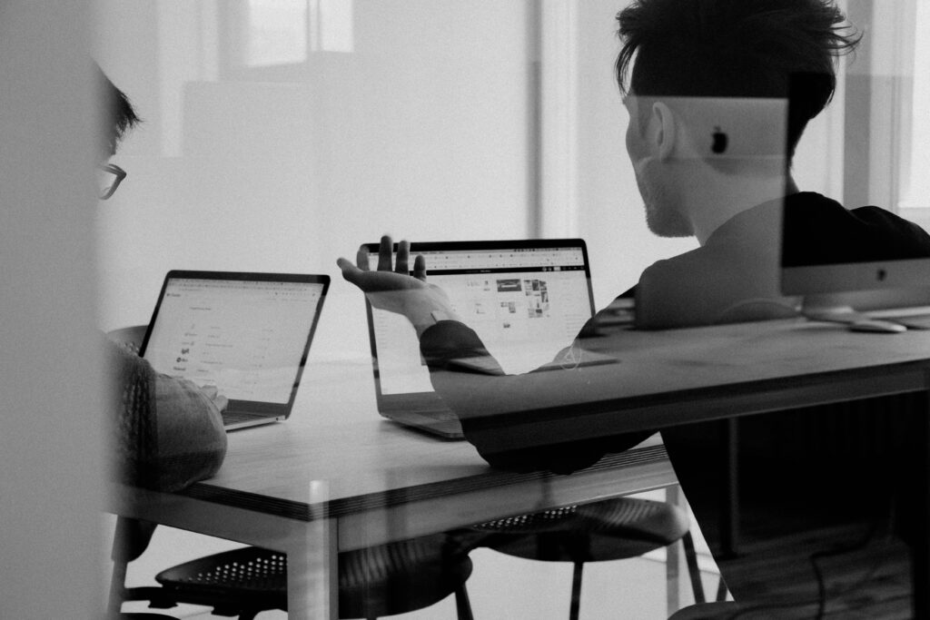 Two professionals collaborating on laptops in an office, discussing energy sector consulting strategies.