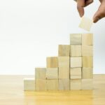 Hand placing a wooden block on a growing stack, illustrating the process of understanding capital raising for business development.