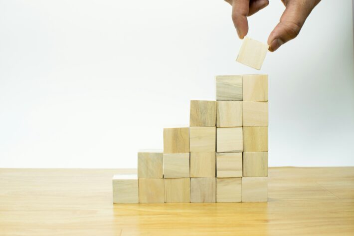 Hand placing a wooden block on a growing stack, illustrating the process of understanding capital raising for business development.