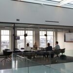 Four professionals in a modern glass meeting room, discussing strategy, representing the psychology of investors in decision-making.