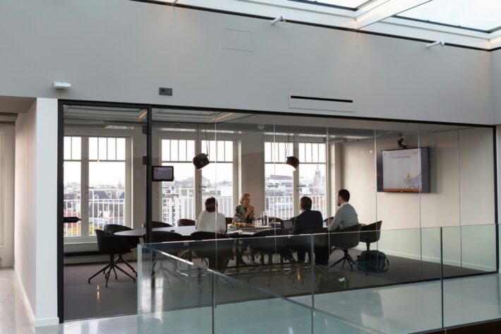 Four professionals in a modern glass meeting room, discussing strategy, representing the psychology of investors in decision-making.